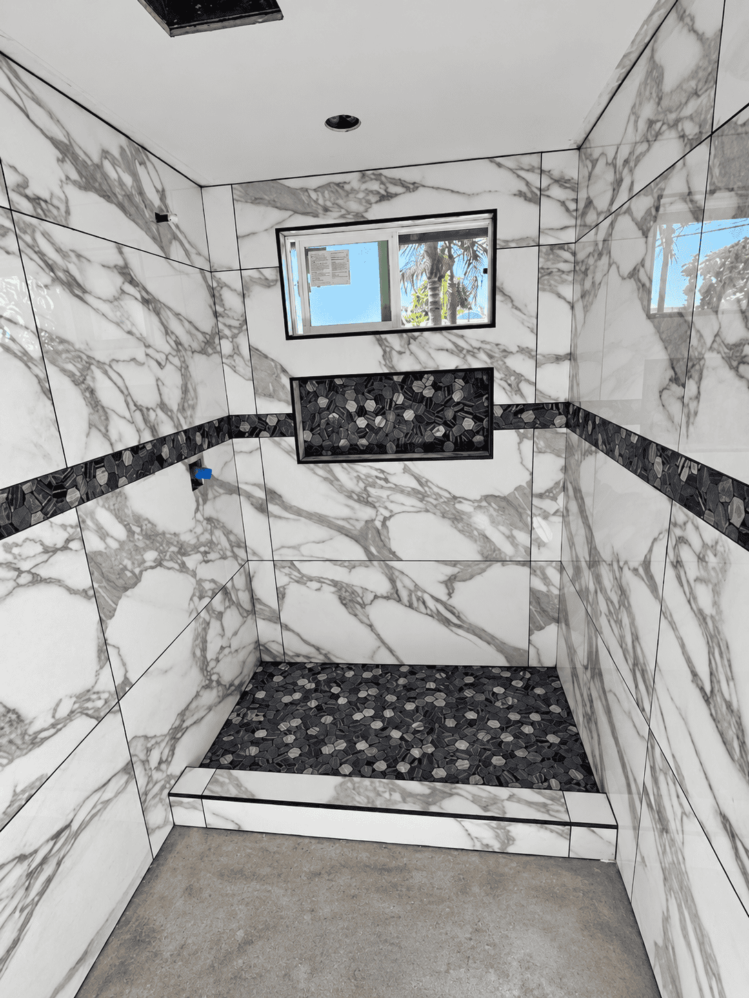 Elegant marble shower with black pebble floor and window.